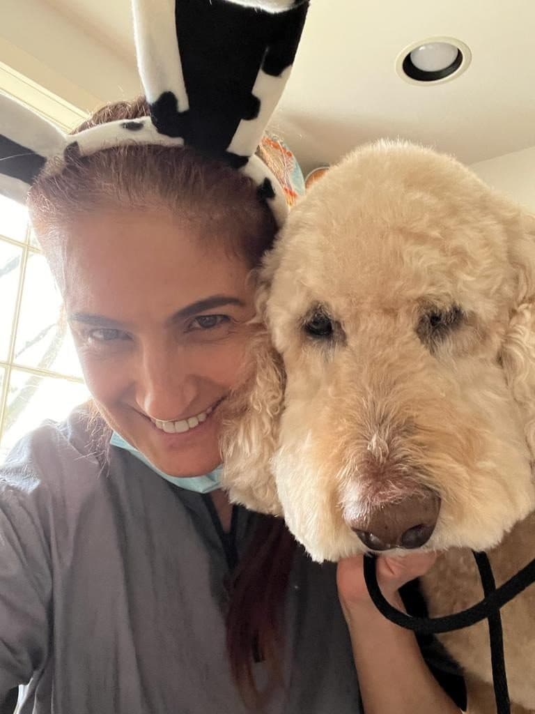Soraya, in cow-print bunny ears, smiling cheek to cheek with a golden doodle
